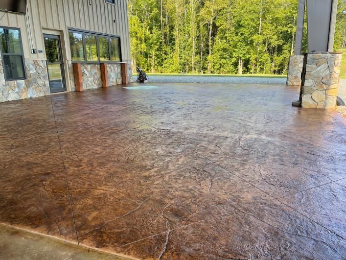 House with porch and brick steps, leading to a stamped concrete patio, construction site. House with a brick patio and steps, wooden porch, and gray exterior.