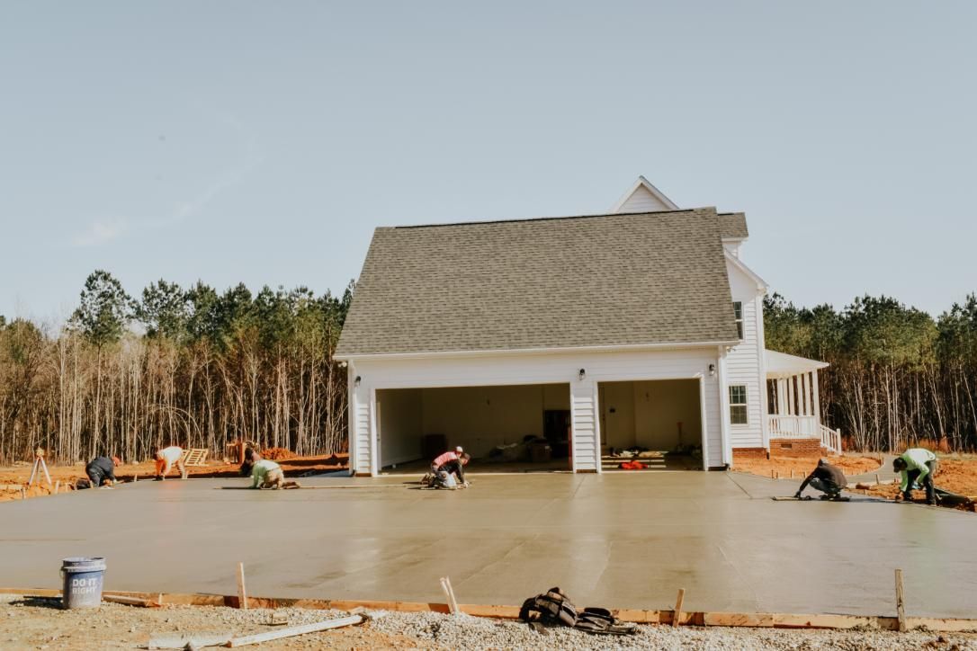 Construction workers smoothing wet concrete driveway in front of a house with two garage doors. Construction workers smoothing wet concrete driveway in front of a house with a two-car garage.
