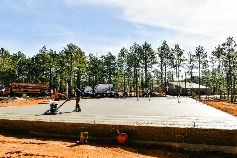 Concrete slab being poured at a construction site, with trees and equipment in the background.