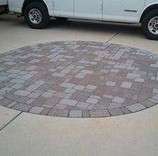 Circular brick paver patio on concrete, with a white vehicle in the background.