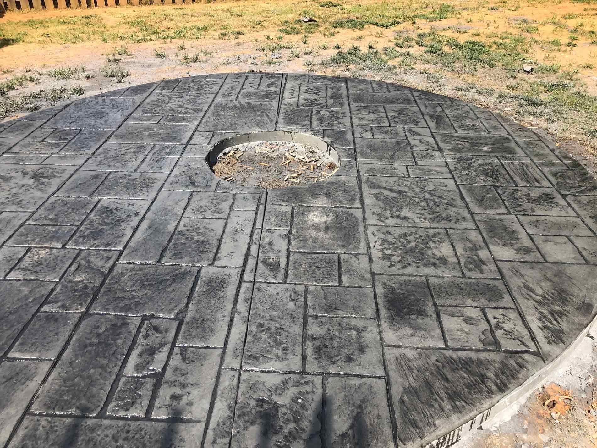 Circular concrete patio with rectangular and square imprints, a central opening, and a grassy background.