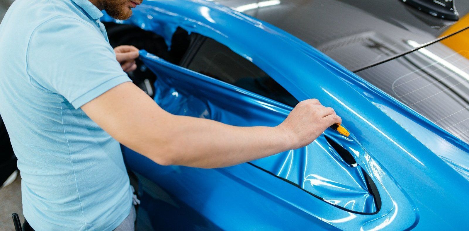 A man is wrapping a blue car with a blue wrap.
