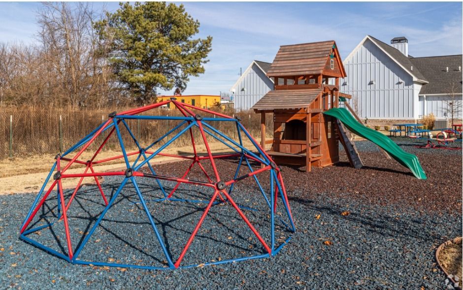 playground with gravel floor, red and blue climbing dome, and a wooden playscape with green slide.
