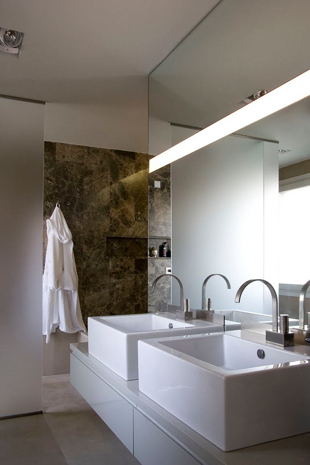 bagno moderno con vista di due lavabi a forma quadrata separati, sulla destra uno specchio e di fronte un accappatoio bianco appeso