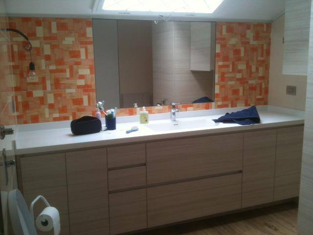 bagno con piastrelle arancioni, specchiera, lavabo centrale con accanto delle trousse e sotto un armadio di color beige