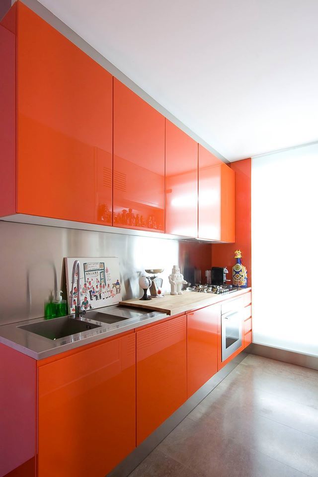 cucina moderna di color arancione vista lateralmente con tagliere e oggetti di porcellana sul pianale, forno in acciaio in basso e sulla sinistra il lavandino
