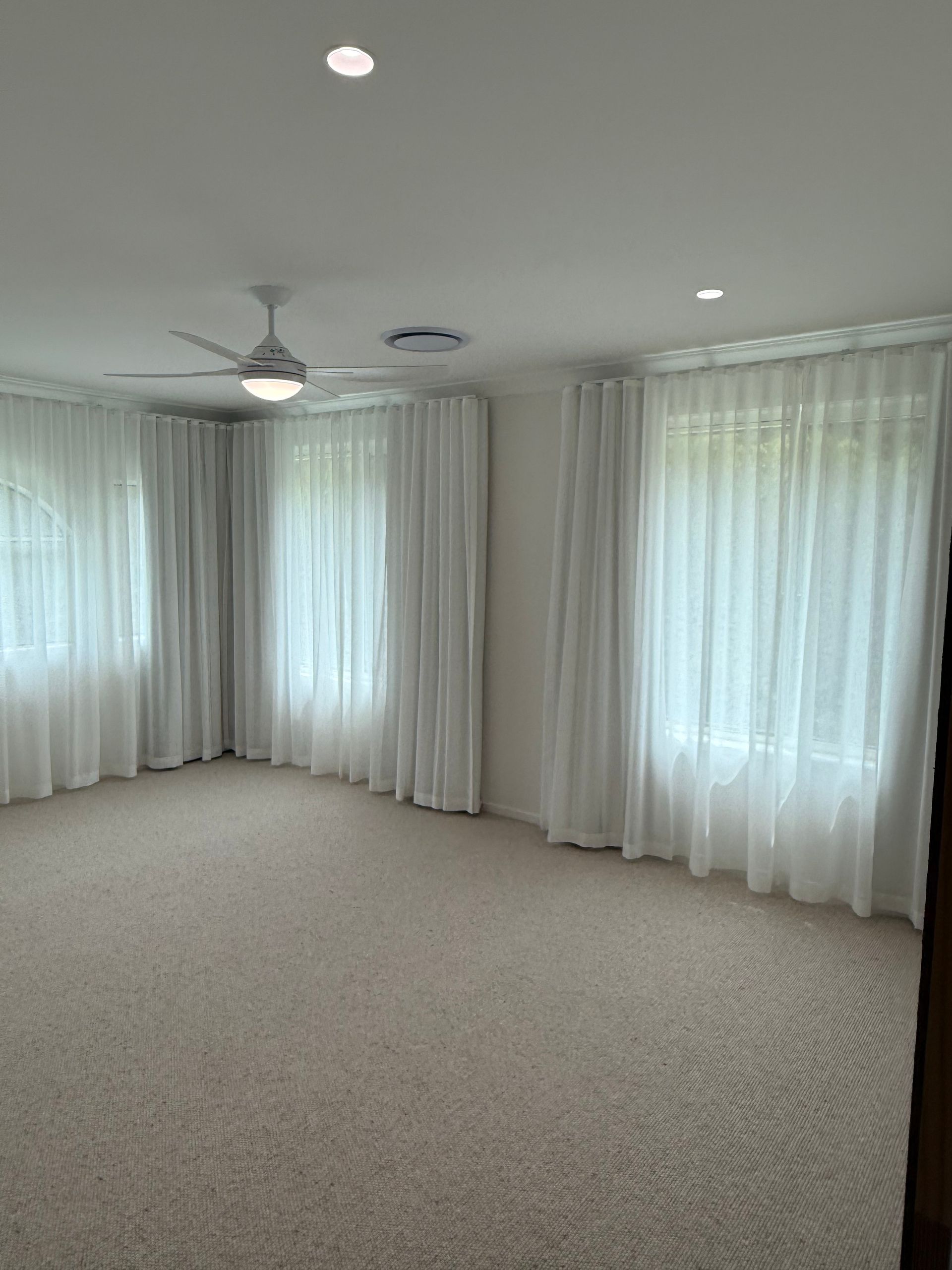 Empty room with beige carpet, white curtains, ceiling fan, and recessed lighting.