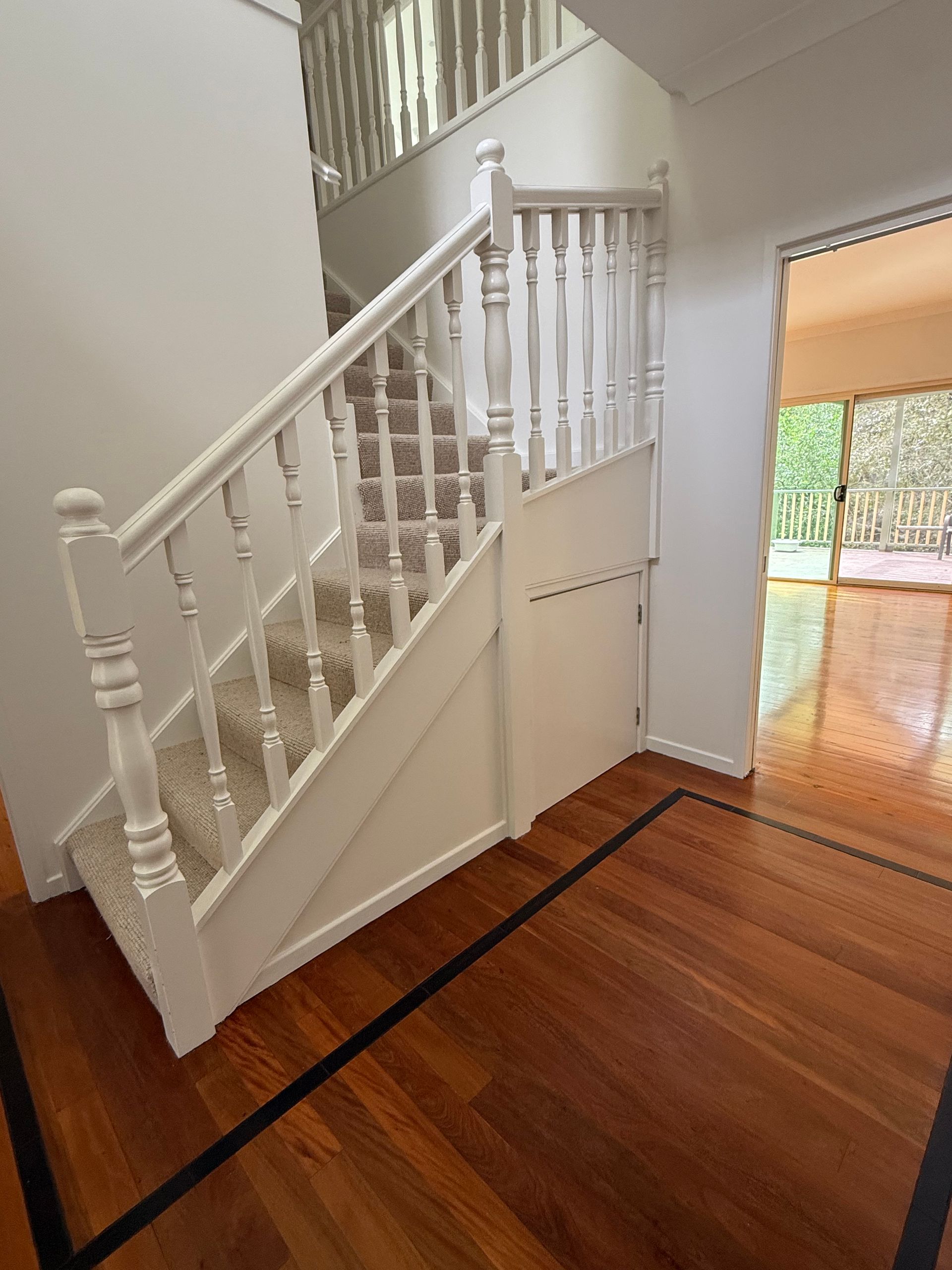 Staircase with carpeted steps and white railing, wooden floor, doorway to another room.