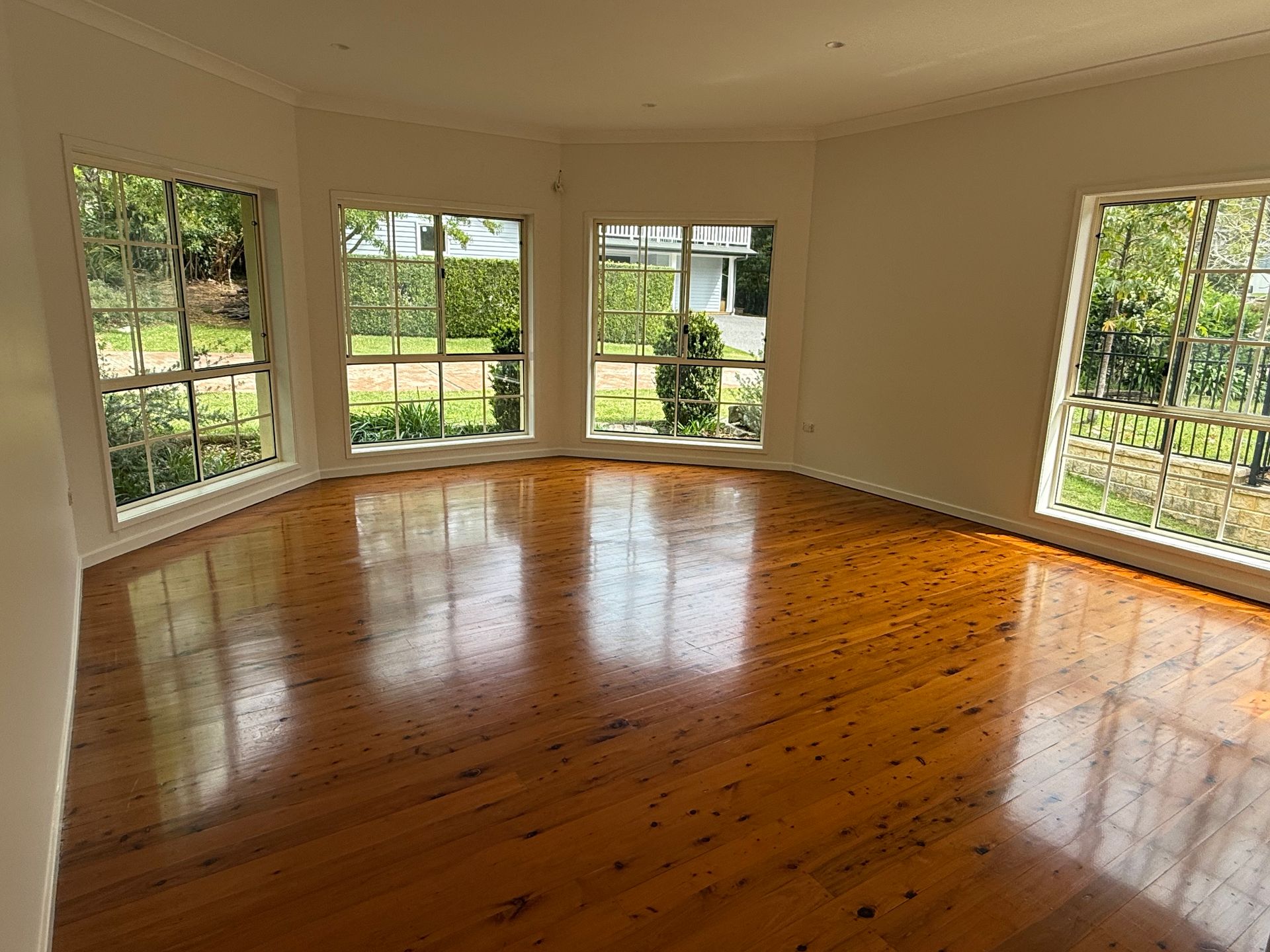 Empty room with polished wooden floor, surrounded by windows, letting in sunlight.