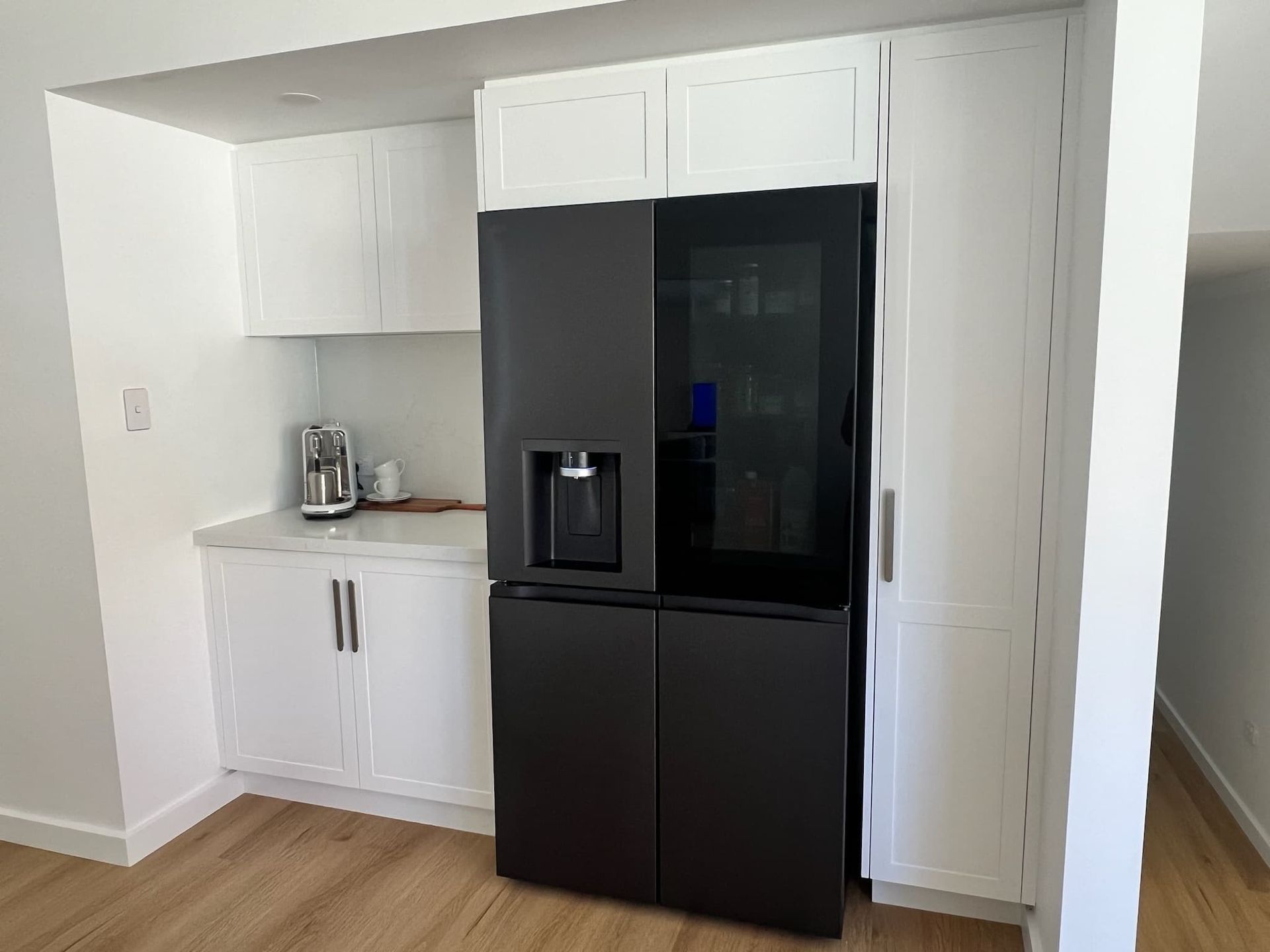 A black refrigerator is sitting in a kitchen with white cabinets — D & J Saverino Painting & Decorating Pty Ltd In Fairy Meadow, NSW
