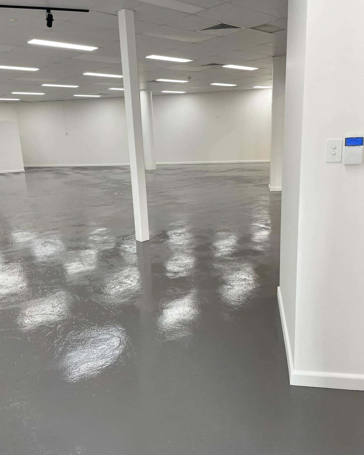 A Large Empty Room With a Gray Floor and White Walls — D & J Saverino Painting & Decorating Pty Ltd In Fairy Meadow, NSW