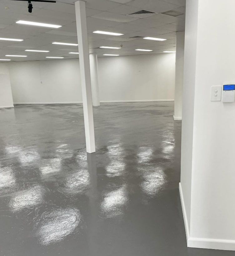 A Large Empty Room With a Gray Floor and White Walls — D & J Saverino Painting & Decorating Pty Ltd In Fairy Meadow, NSW