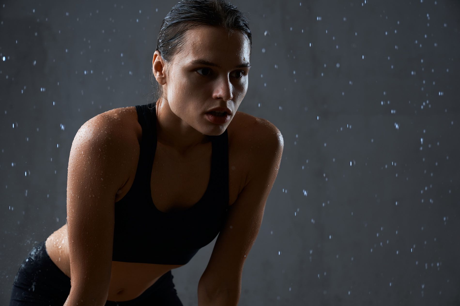 A person in athletic gear stands with a focused, weary expression in the rain against a dark background.