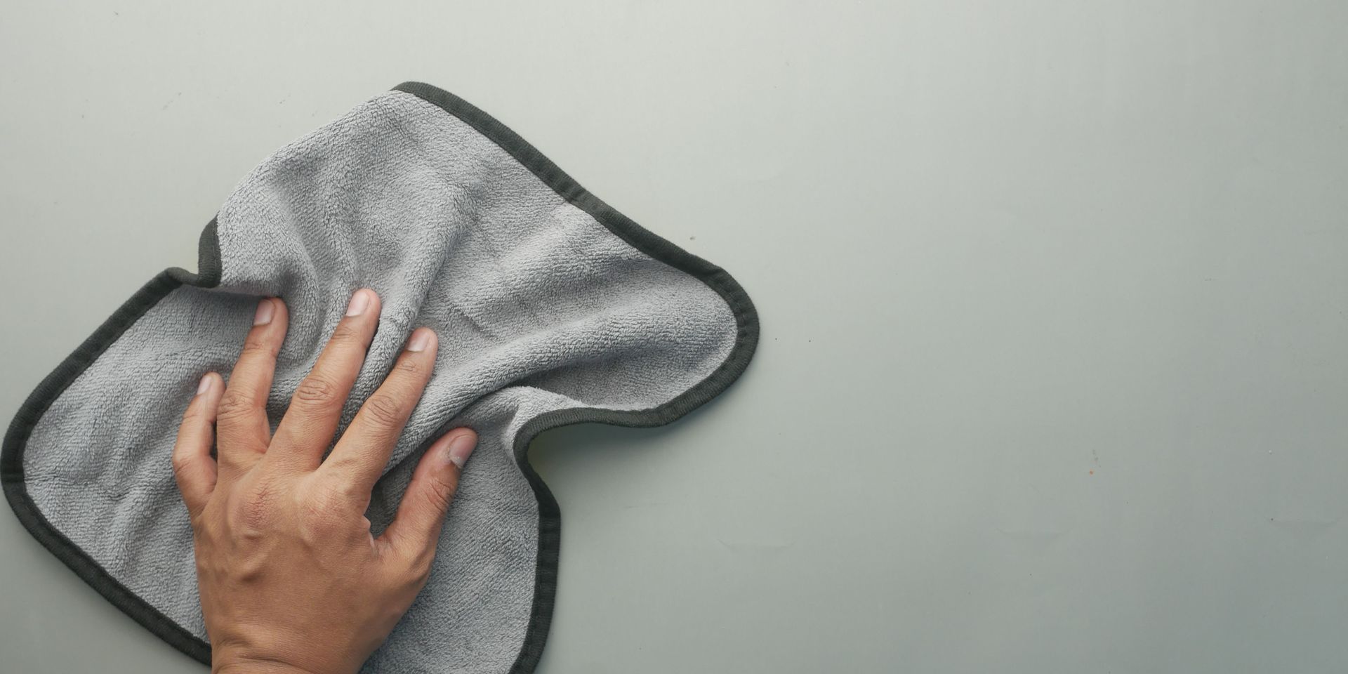 Hand wiping a gray surface with a gray cloth.