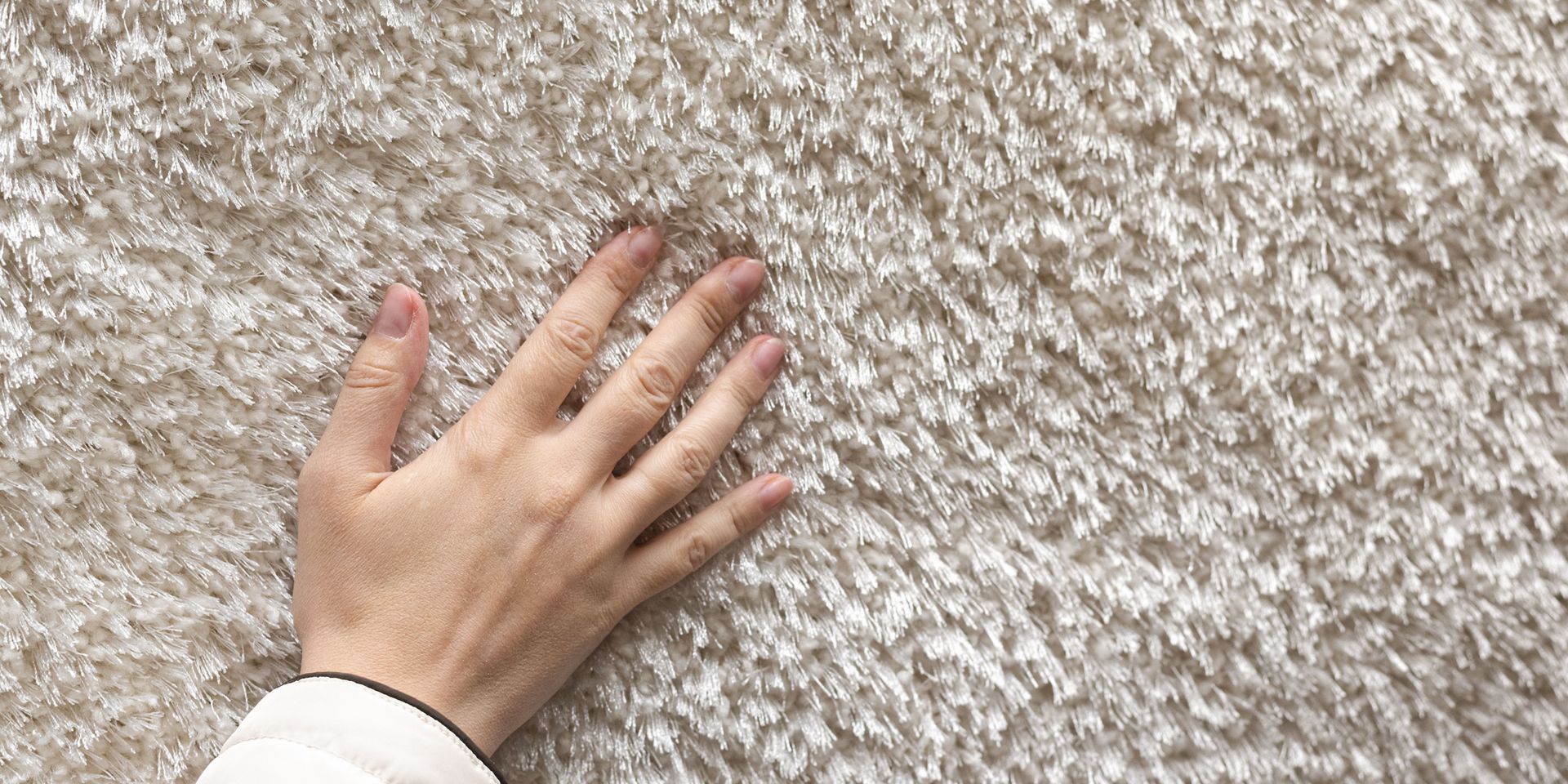 A person 's hand is touching a white carpet.