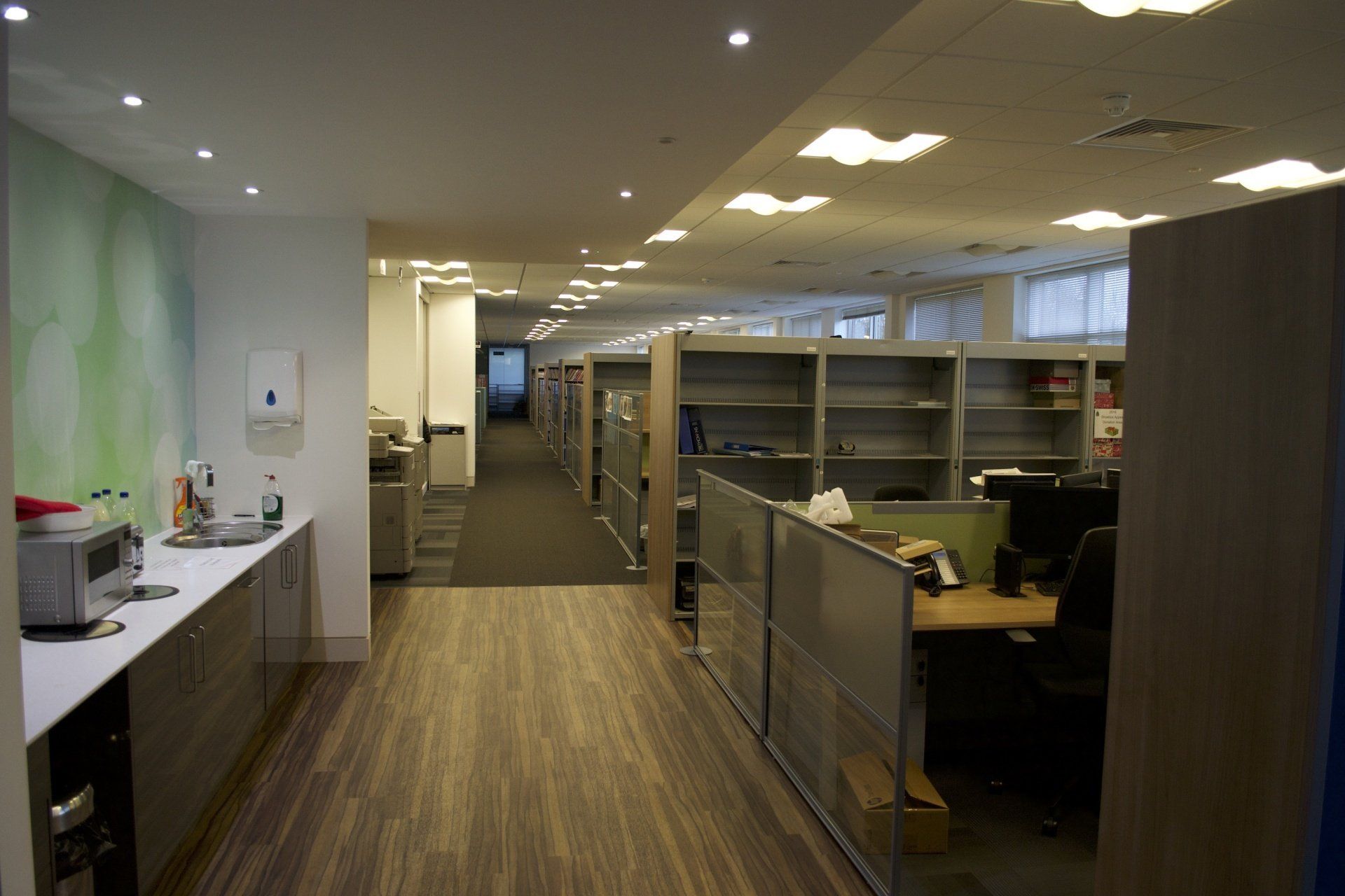 A long hallway in an office with cubicles and desks.
