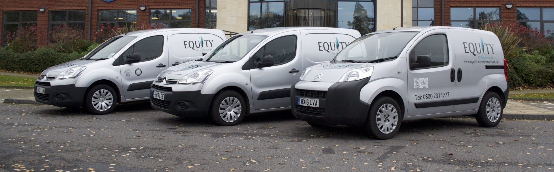 Three white vans are parked in front of a building
