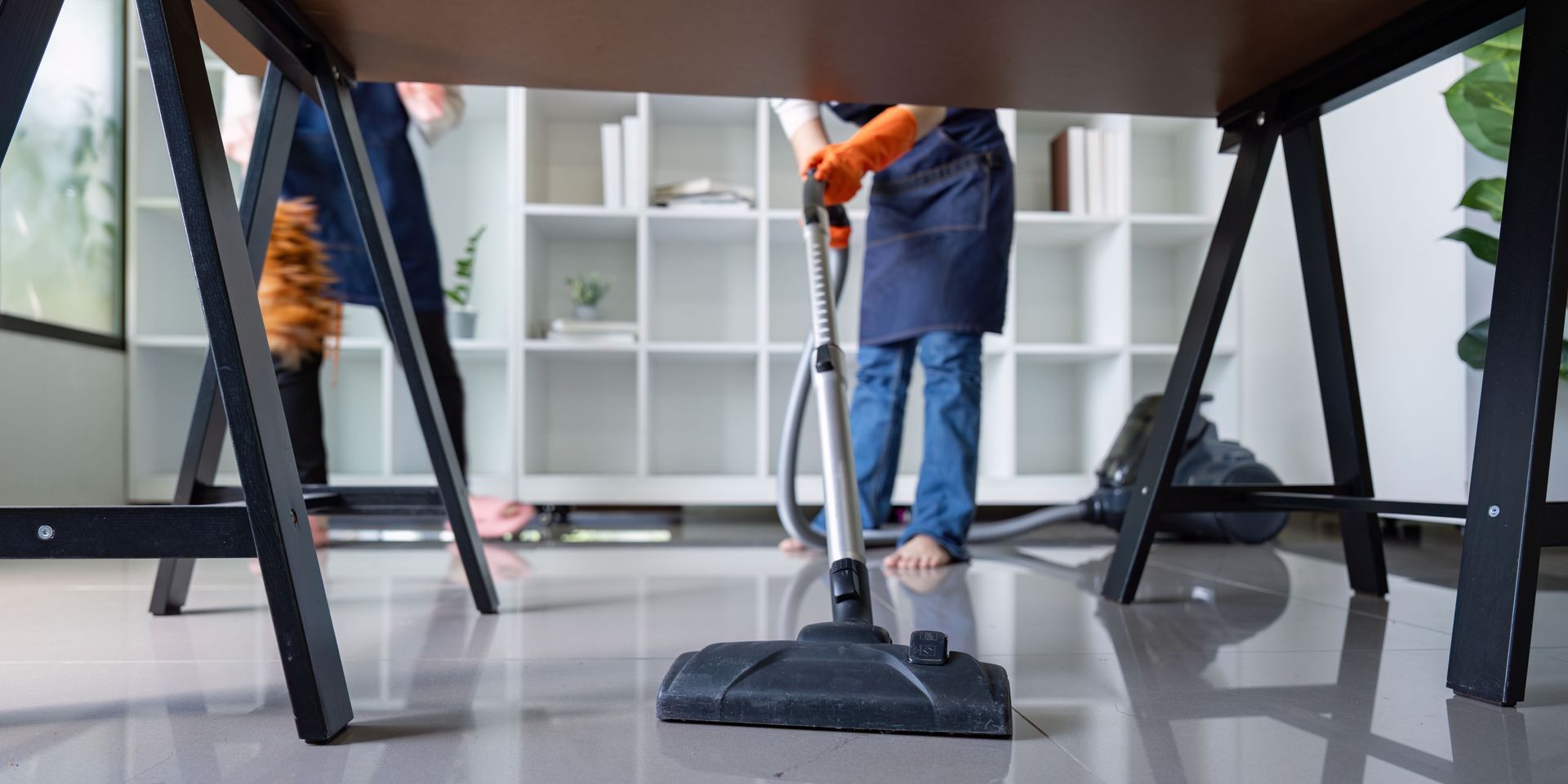 A couple of people are cleaning a room with a vacuum cleaner.