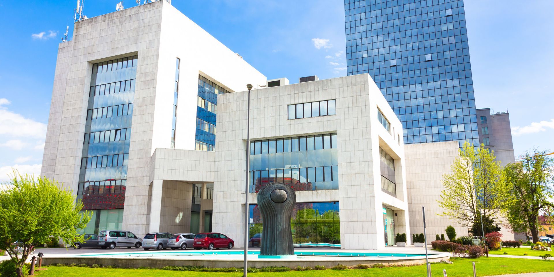 Exterior of a modern building with a large sculpture and a blue glass skyscraper in the background.