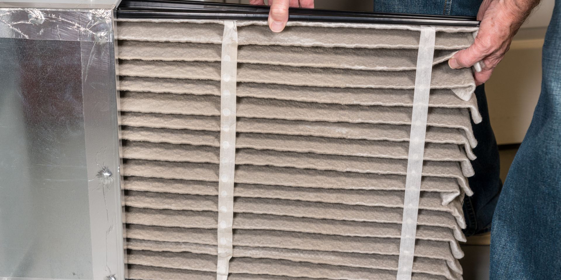 Person removing a dirty air filter from a metal housing.