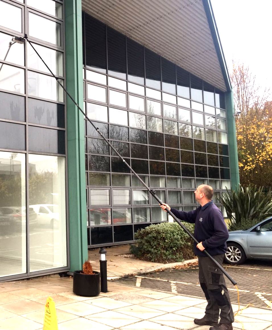 A man is cleaning the windows of a building with a long pole.