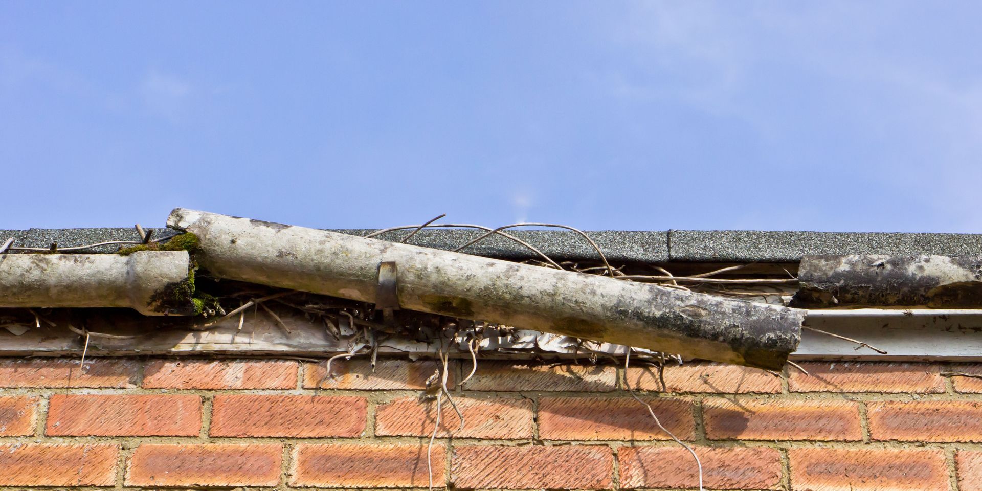 A broken gutter on a brick wall with a blue sky in the background.