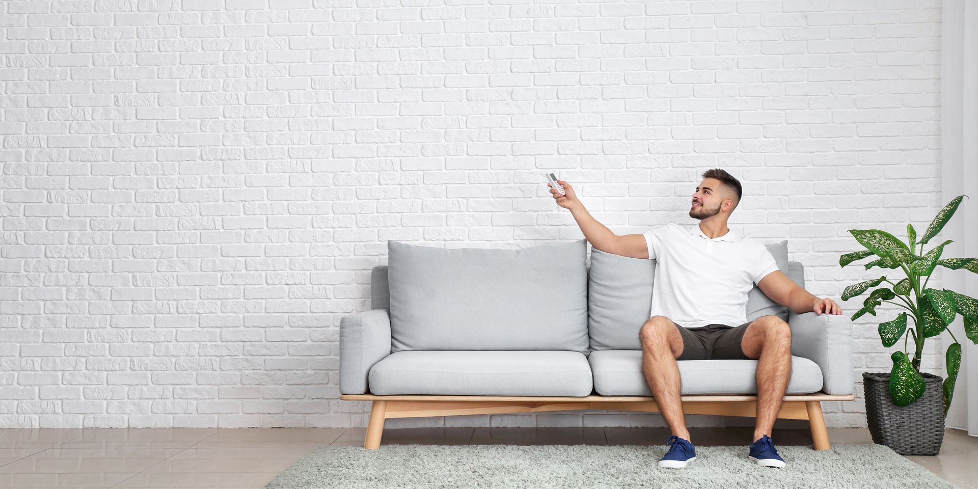 A man is sitting on a couch in a living room holding a remote control.