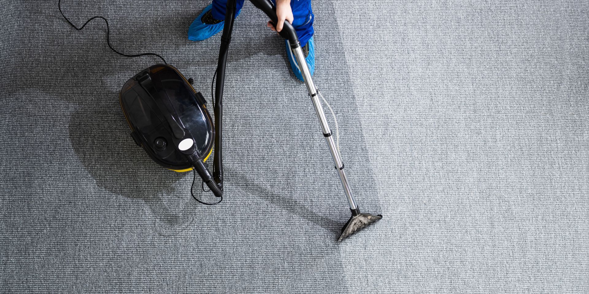 A person vacuuming a gray carpet with a black vacuum cleaner.