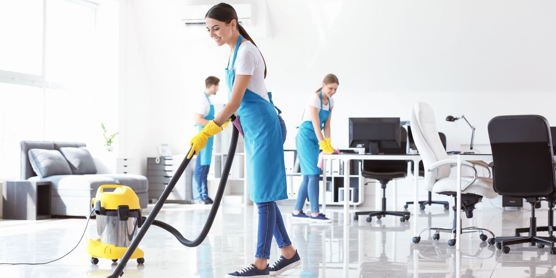 A woman is using a vacuum cleaner to clean an office floor.