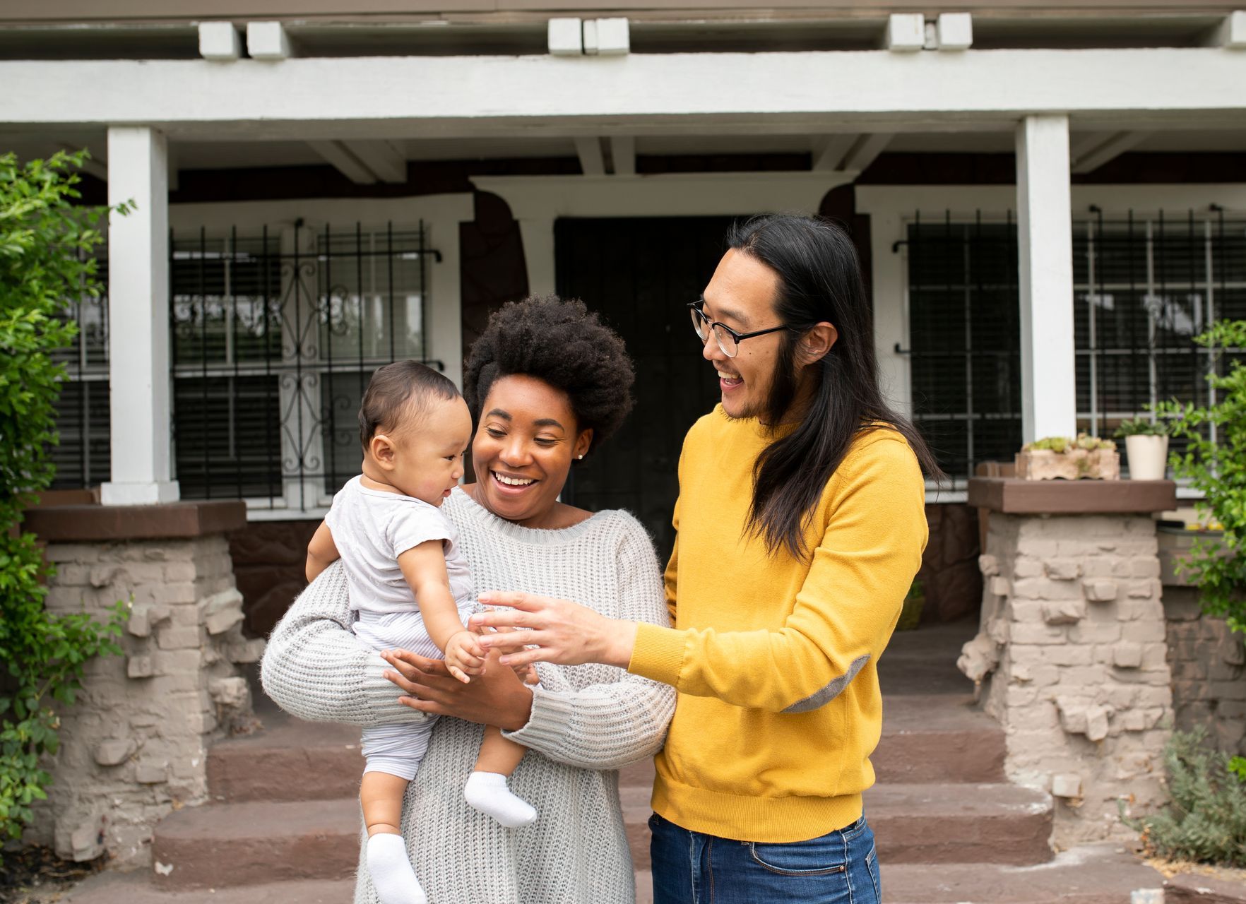 A man and woman are holding a baby in front of a house.