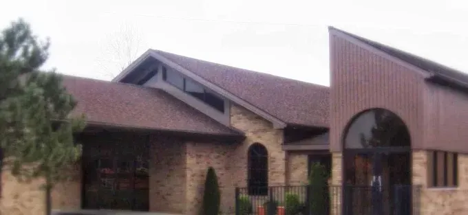 A brick building with a brown roof and arched entrance. A large tree sits to the left of the building.