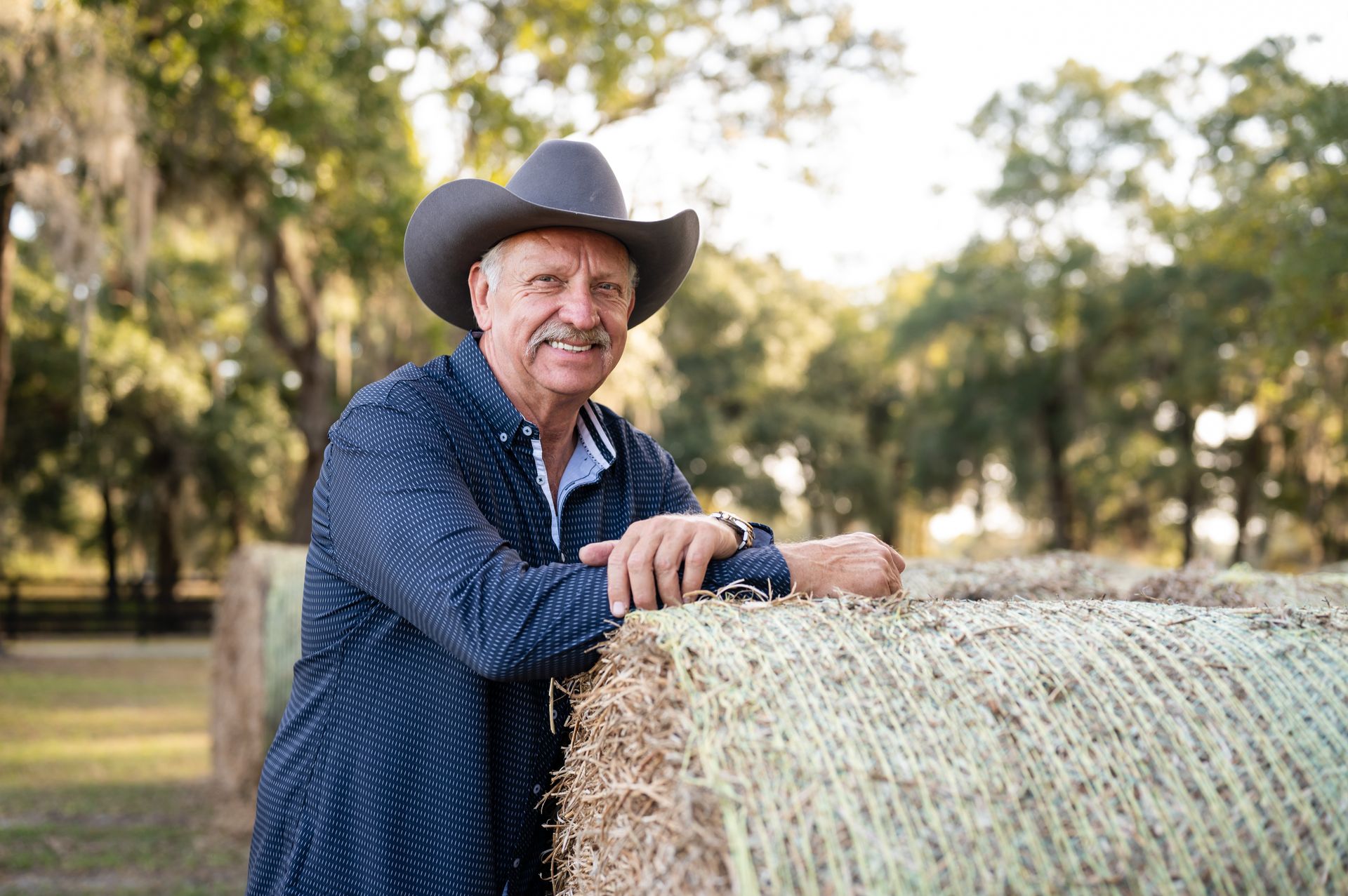 A man in a cowboy hat is leaning on a bale of hay.