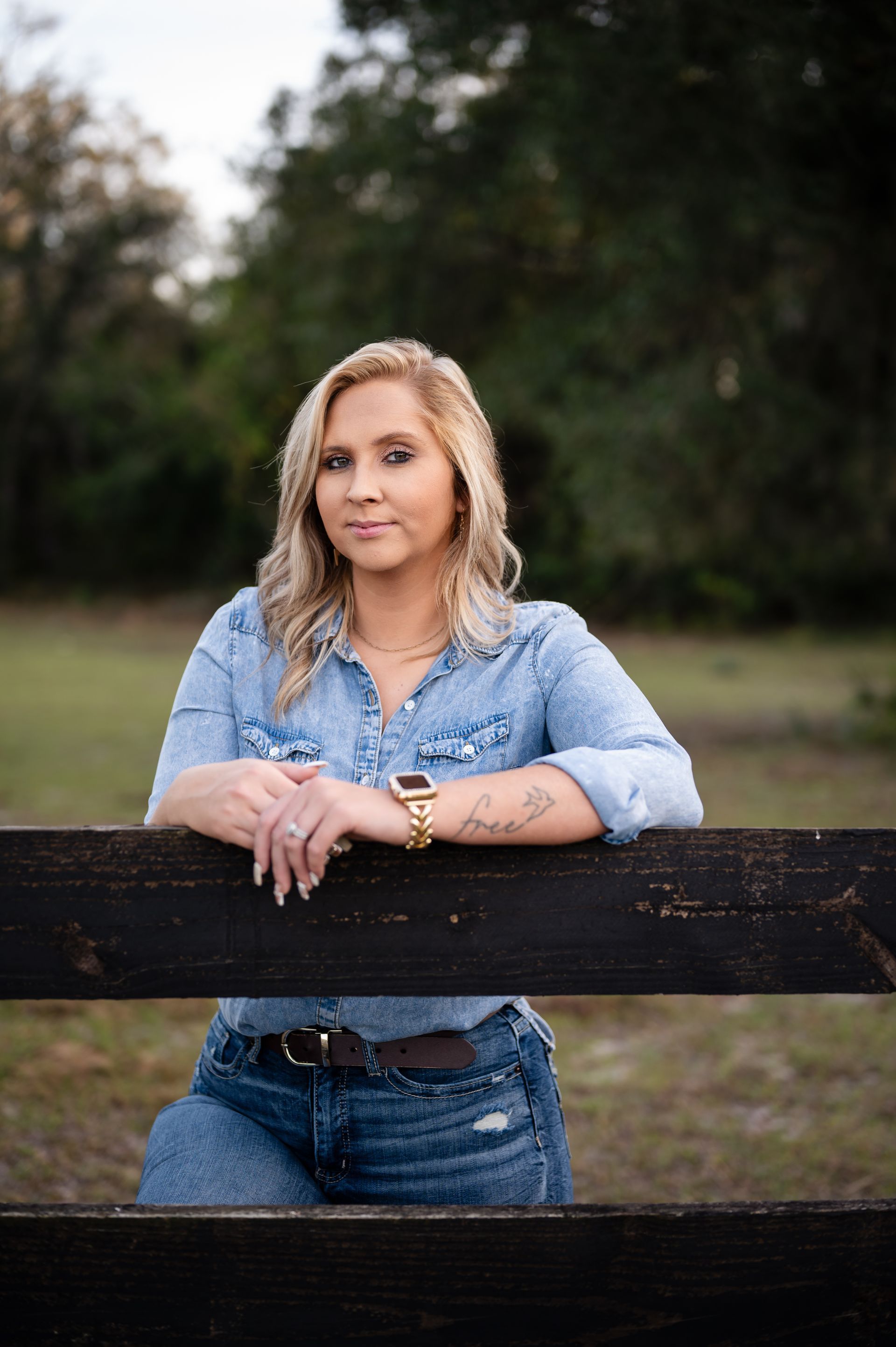 A woman leaning on a wooden fence in a field.