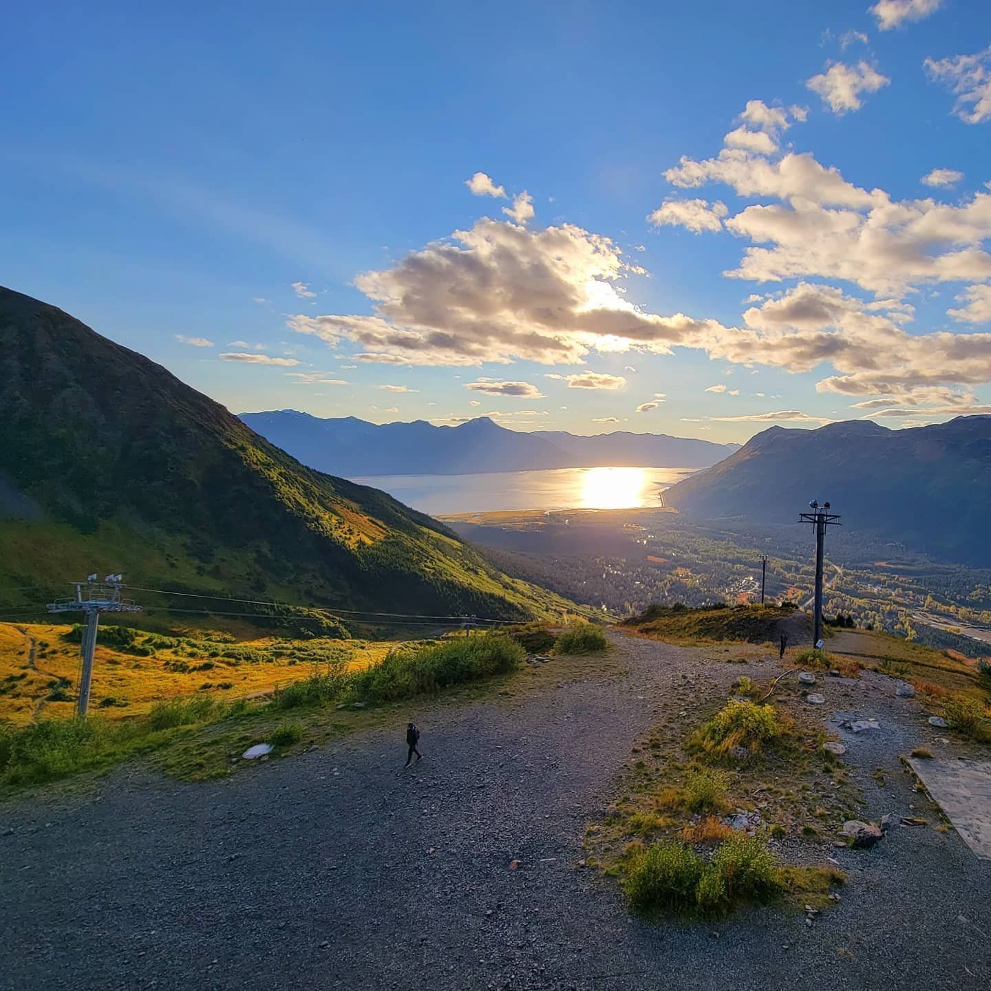 Mountain vista with person, sunset over water, blue sky.