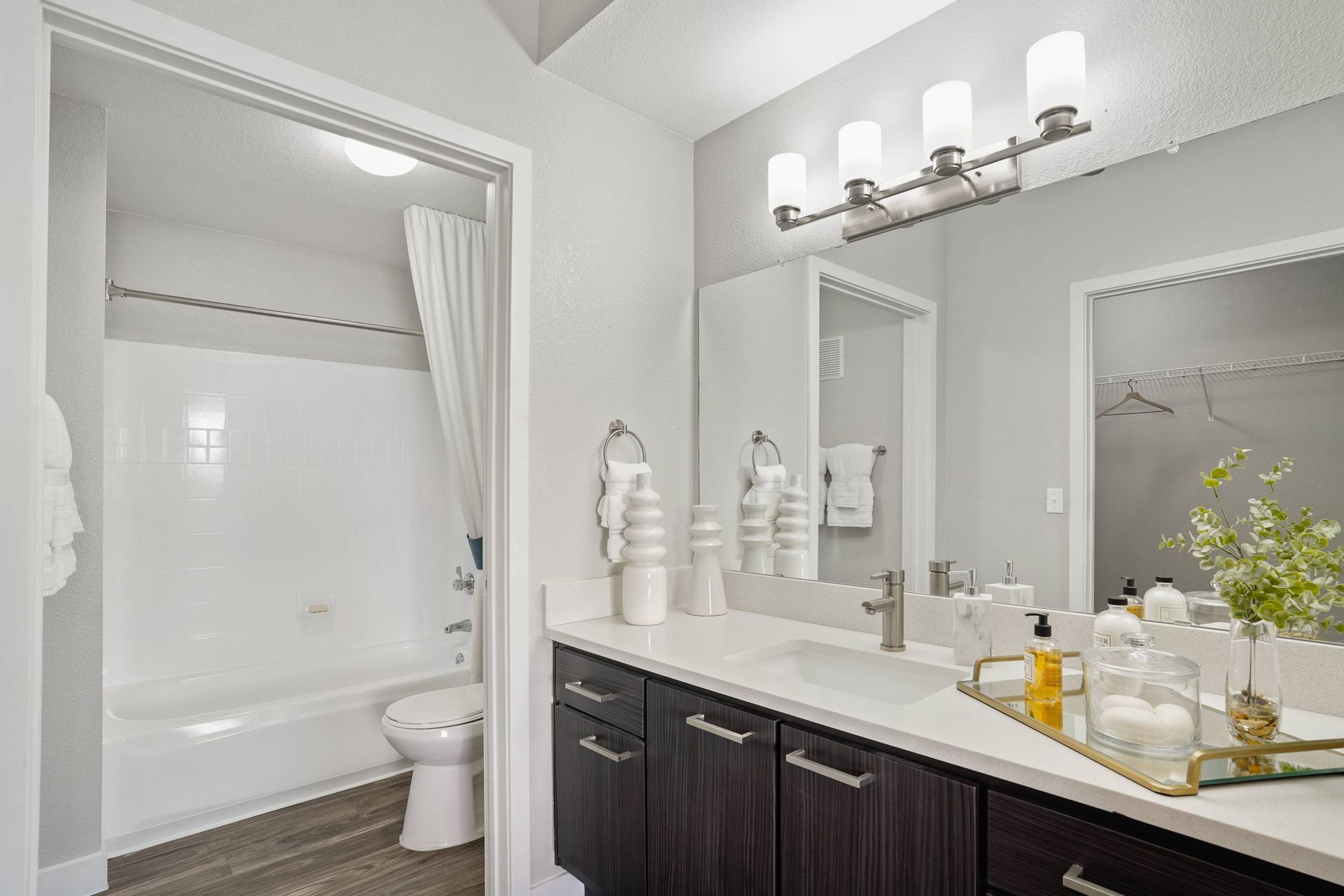 Bathroom featuring a dark wood vanity, white countertop, large mirror, and a tub/shower with white tile.