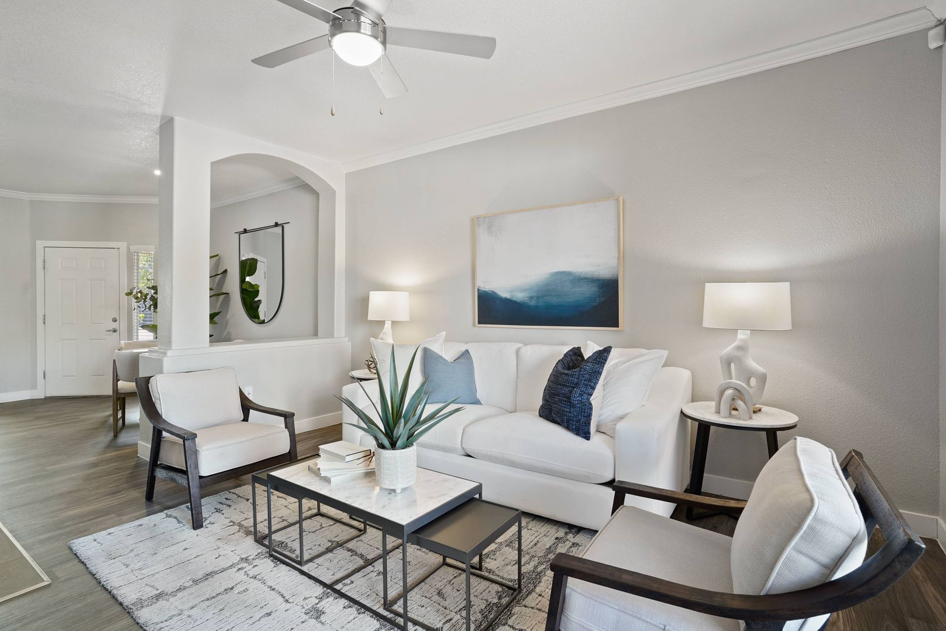 Bright living room in a modern apartment with white sofa, two armchairs, and a coffee table.