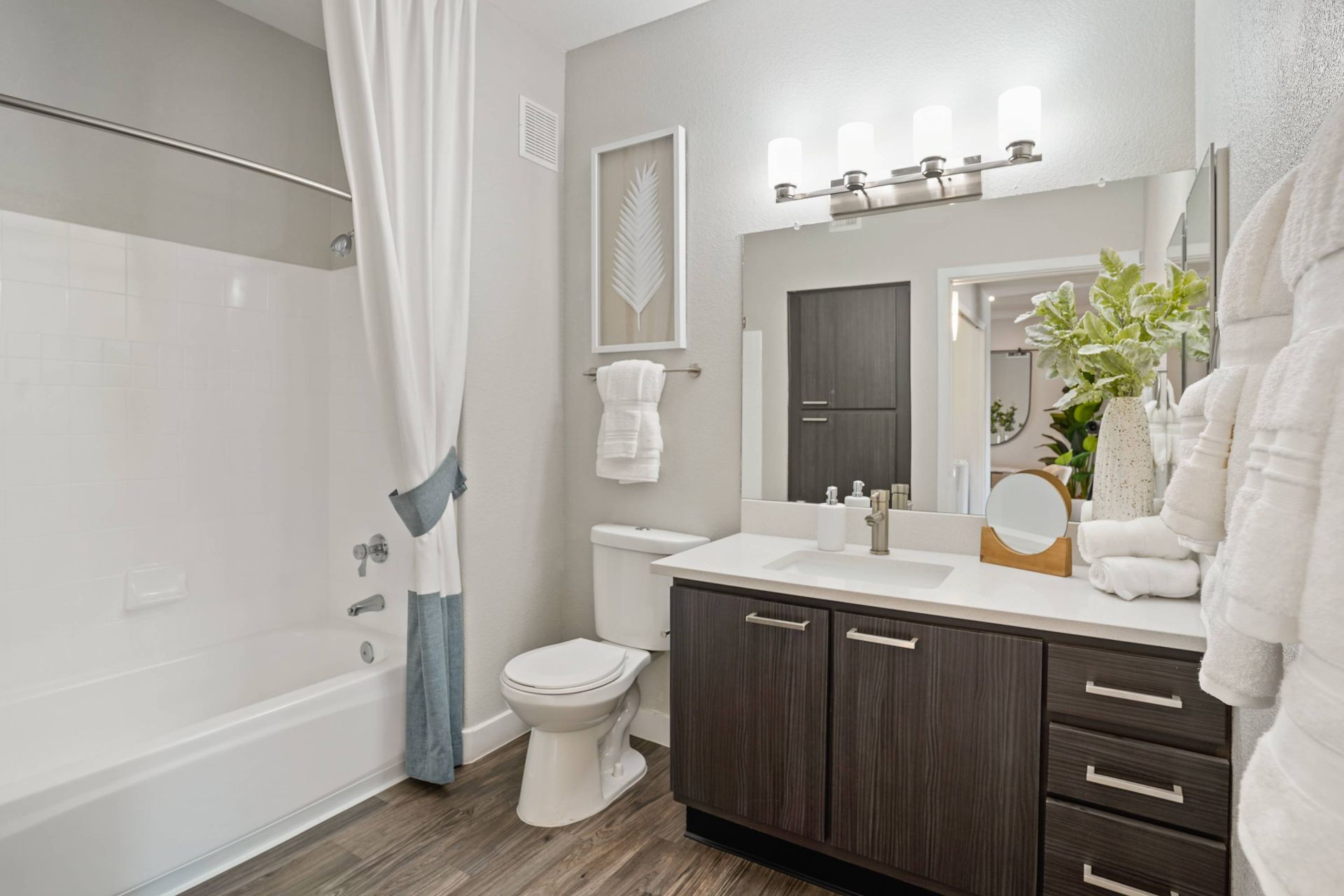 Modern apartment bathroom with vanity, sink, mirror, towels, and a tub/shower.