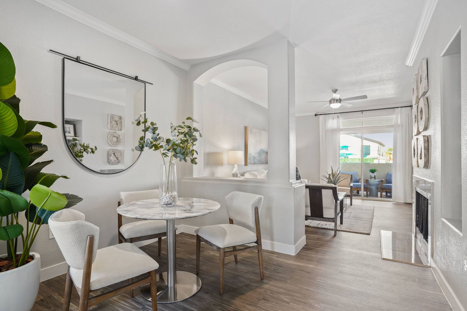 Dining nook with round marble table and four upholstered chairs; living room visible beyond.