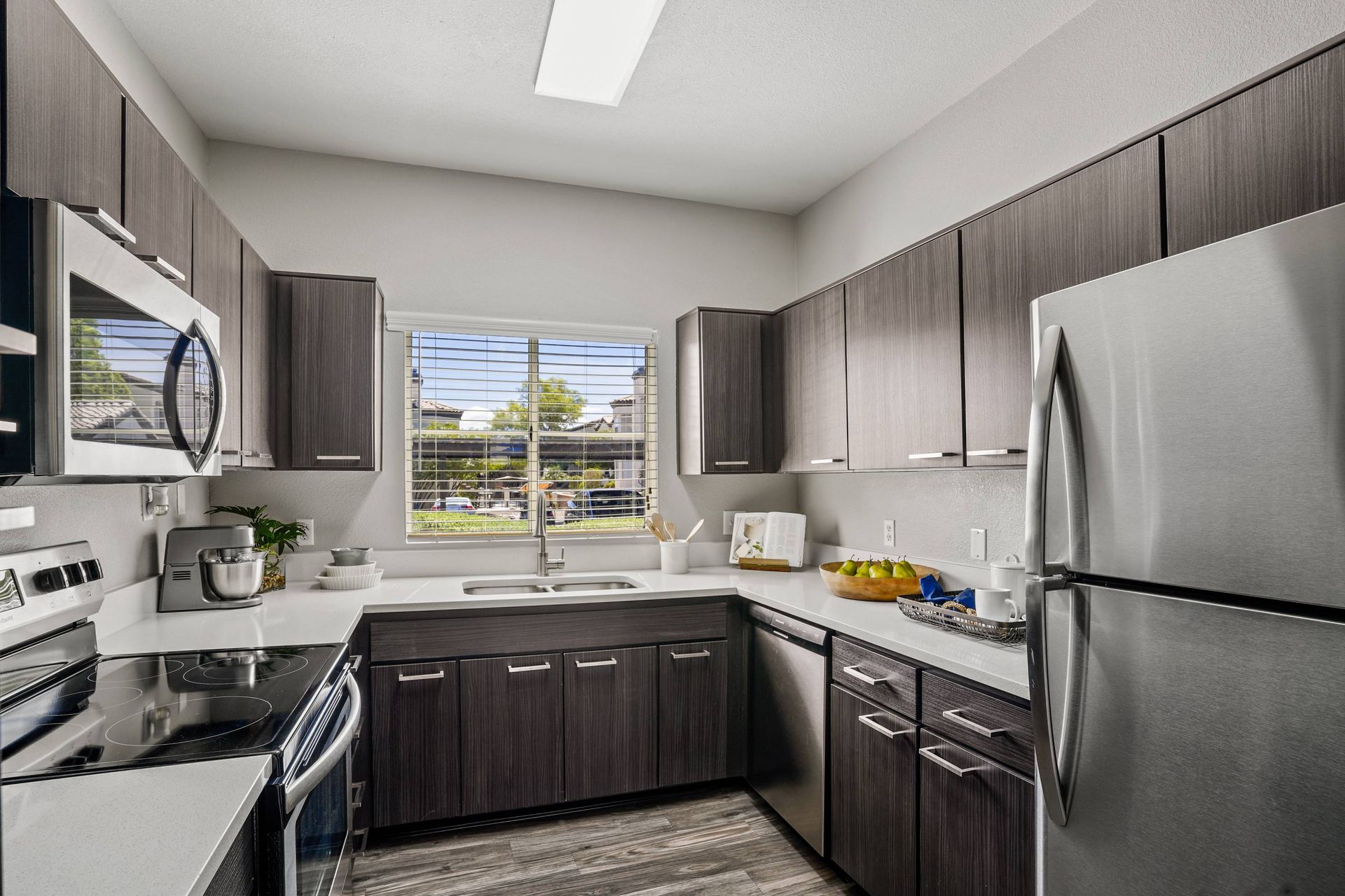 Modern kitchen with dark wood cabinets, stainless steel appliances, and a window over the sink.