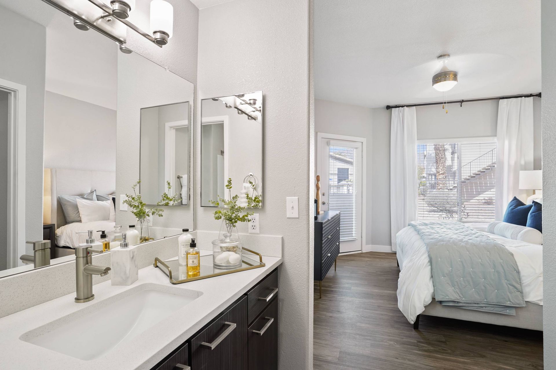 Modern apartment bathroom vanity with double mirrors; leads to bright bedroom.