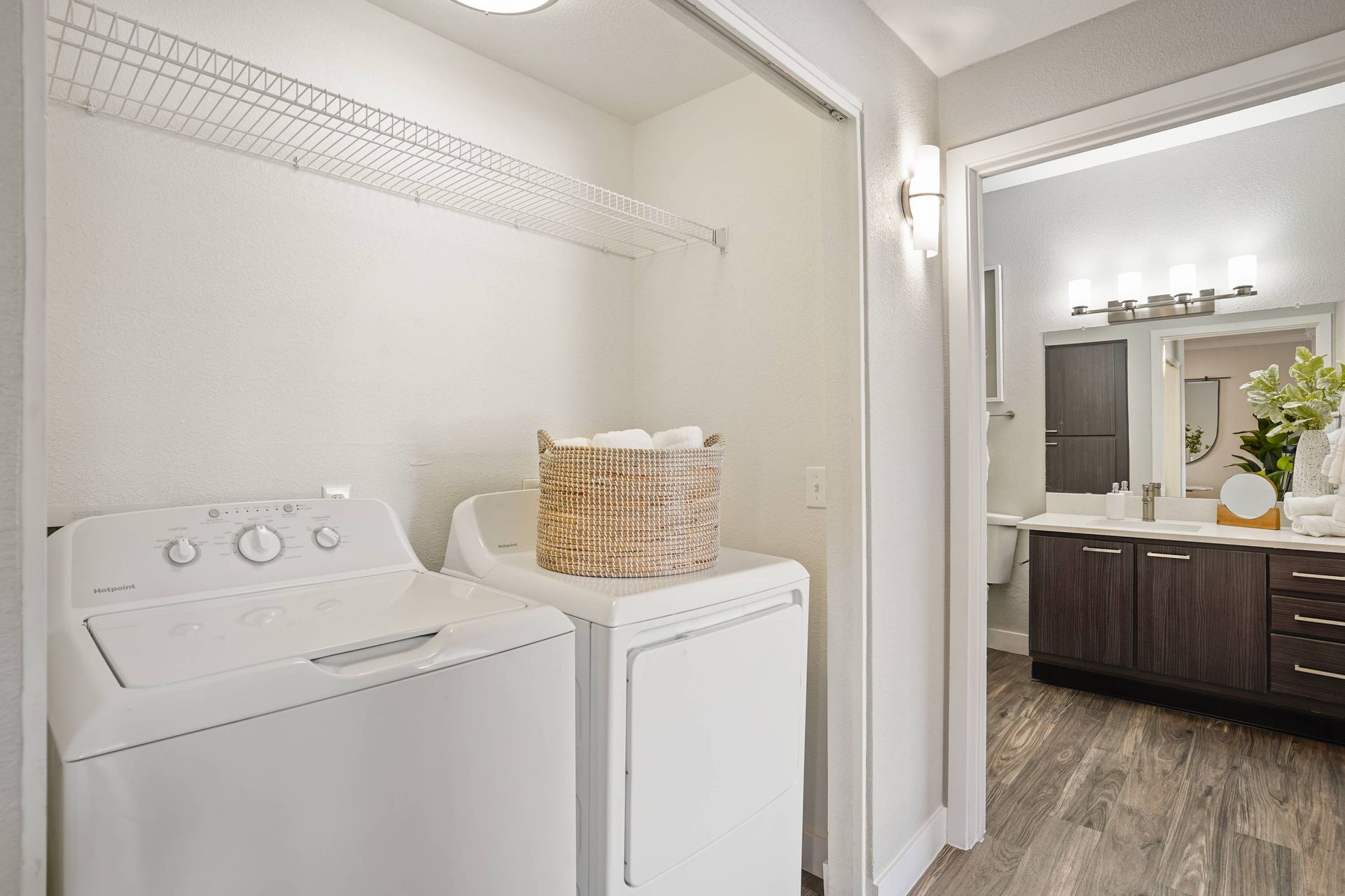 Laundry area with washer and dryer, wire shelf, and doorway to bathroom vanity.