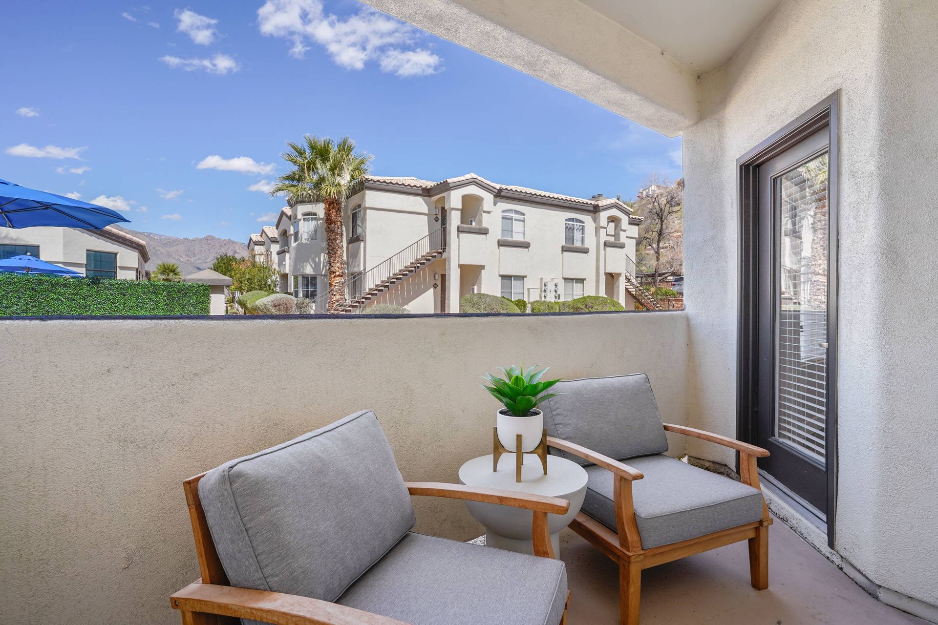 Balcony with two cushioned chairs and a small table overlooking a desert-style apartment complex.