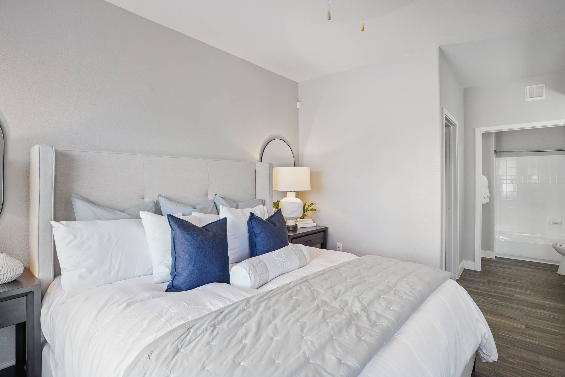 Bedroom in a modern apartment with a tufted headboard, white bedding, and an open bathroom.