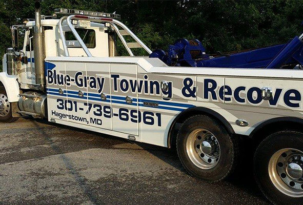 A blue gray towing truck is parked in a parking lot