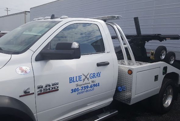 A blue gray tow truck is parked in front of a building