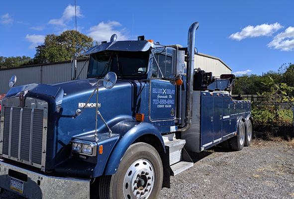 A blue tow truck is parked in a gravel lot.