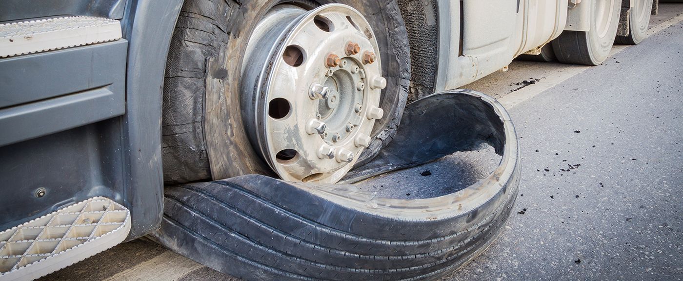 A deflated truck tire on a paved road, revealing the wheel.