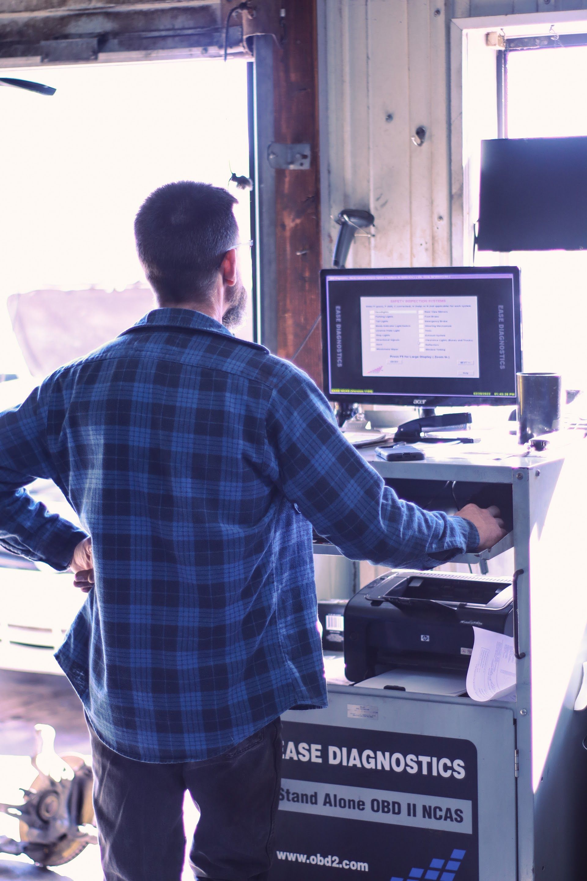Man in blue plaid shirt operates computer at a station | | Lowry Auto Service