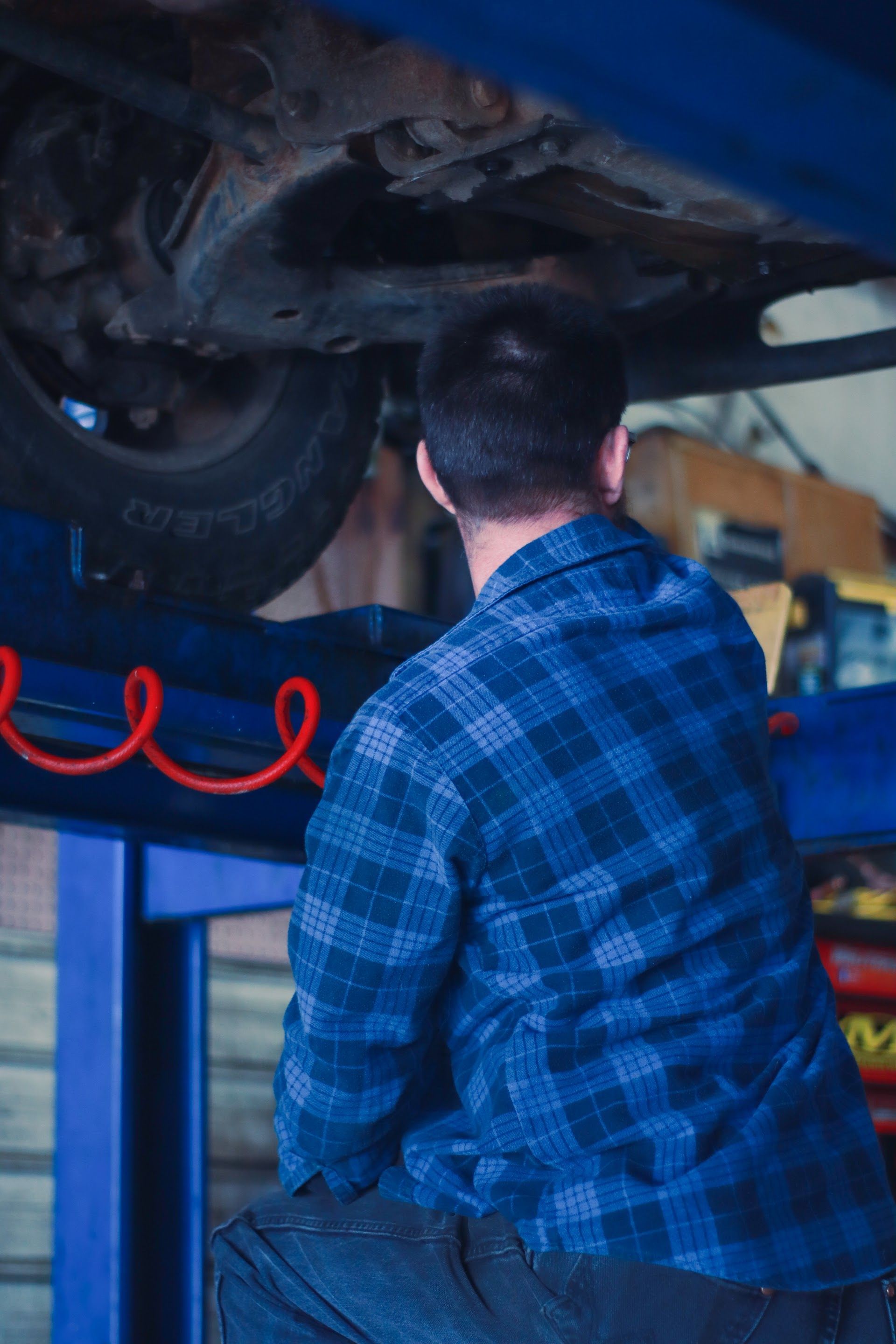 Mechanic in blue plaid shirt working on underside of a car raised on a lift | Lowry Auto Service