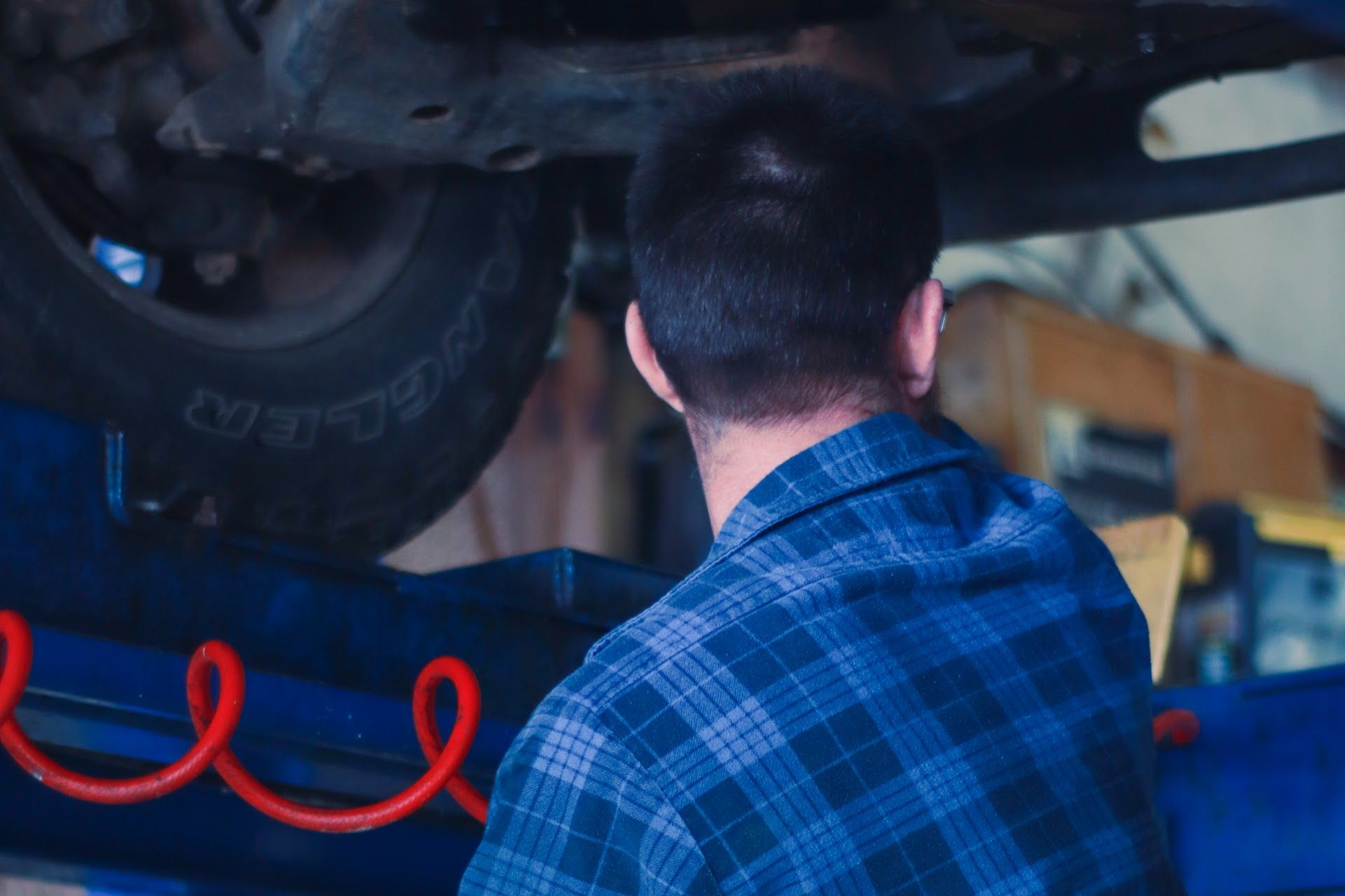 Mechanic in a blue plaid shirt inspecting the underside of a car on a lift | Lowry Auto Service